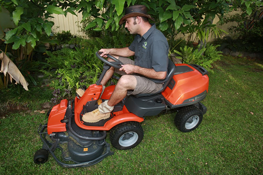 Lawn mowing Mackay — GreenMan operator on a Husqvarna ride-on in a tropical backyard